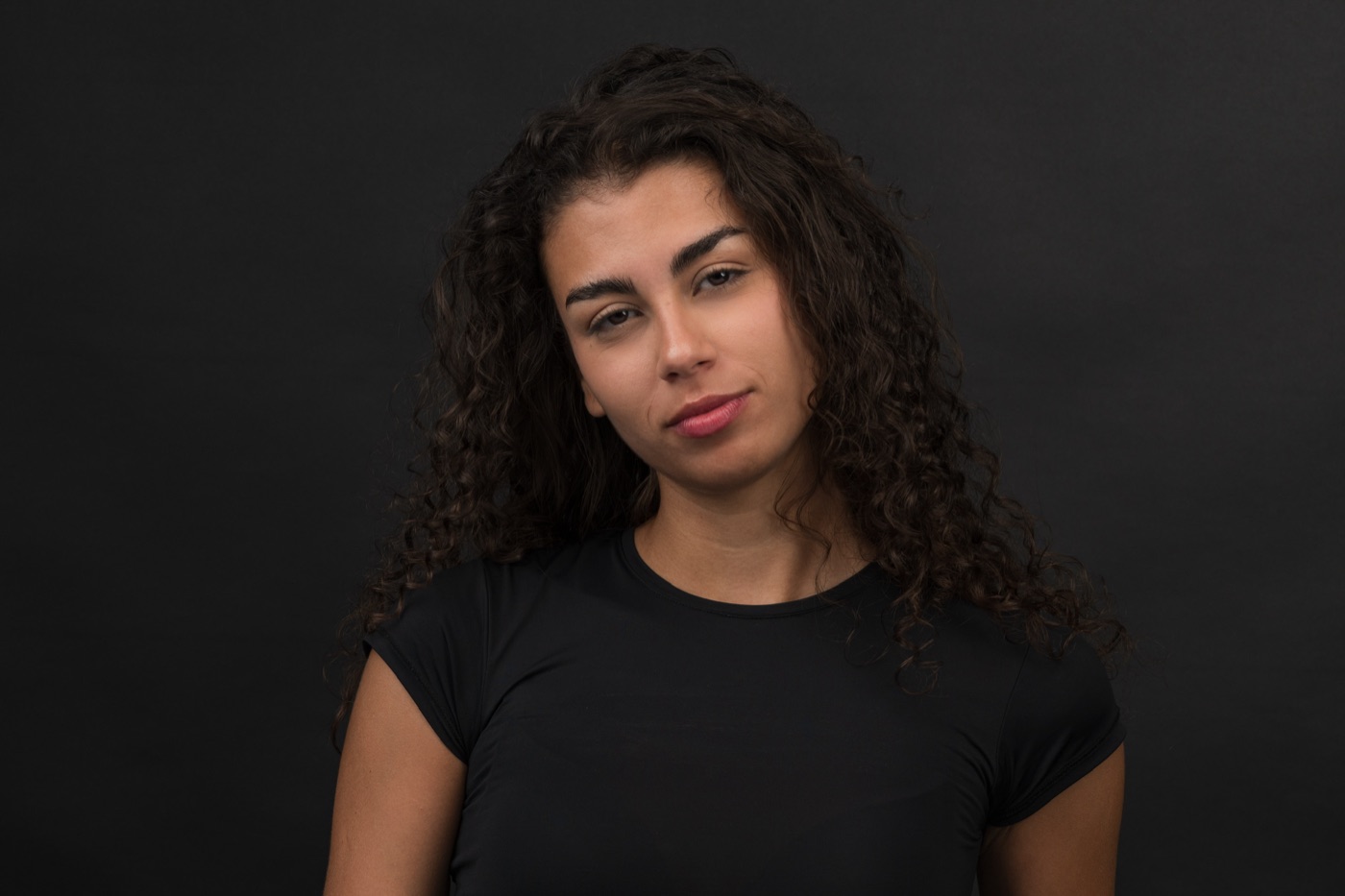 Retrato de Vitoria con la cabeza ladeada y camiseta negra, fondo negro